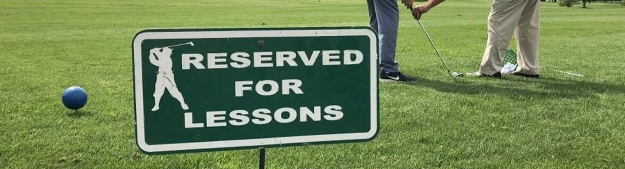 A sign saying "reserved for lessons" with a golf instructor and student in the background